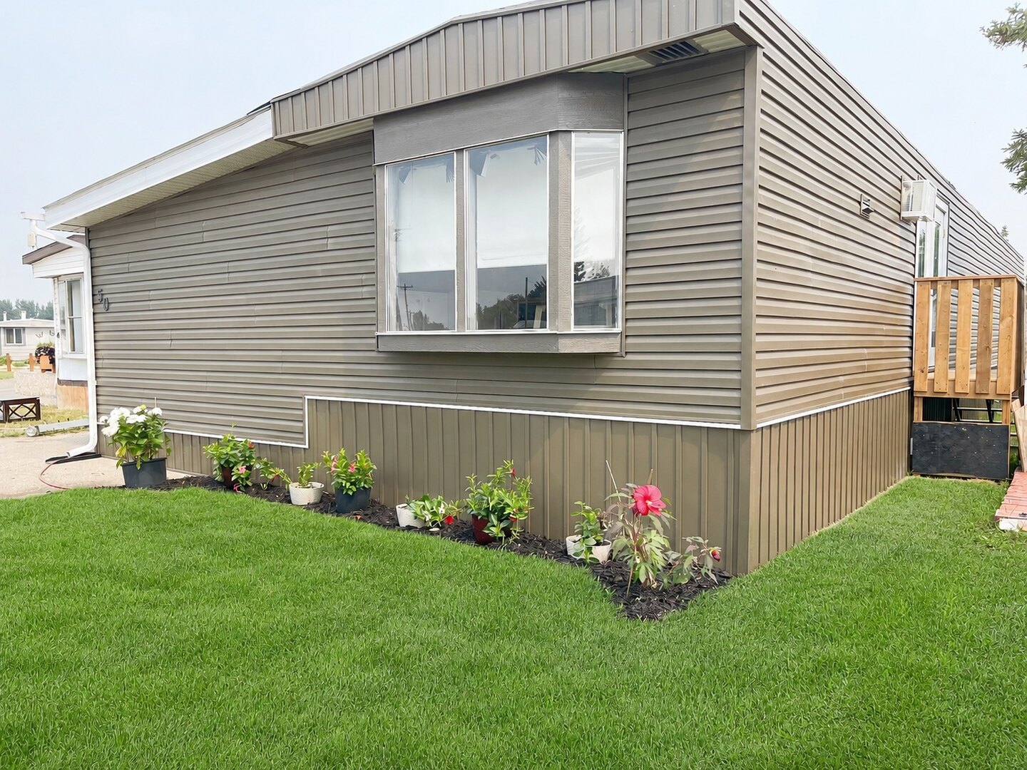 Front corner of the home at #50 5301 2nd Street, showing its bay window, gray siding and lawn